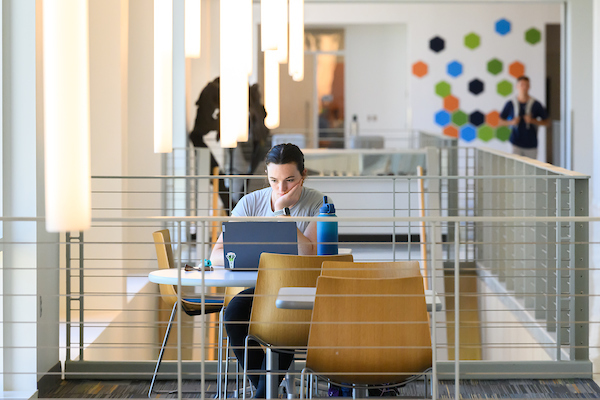 student studying and using a laptop at a table in a common space on campus