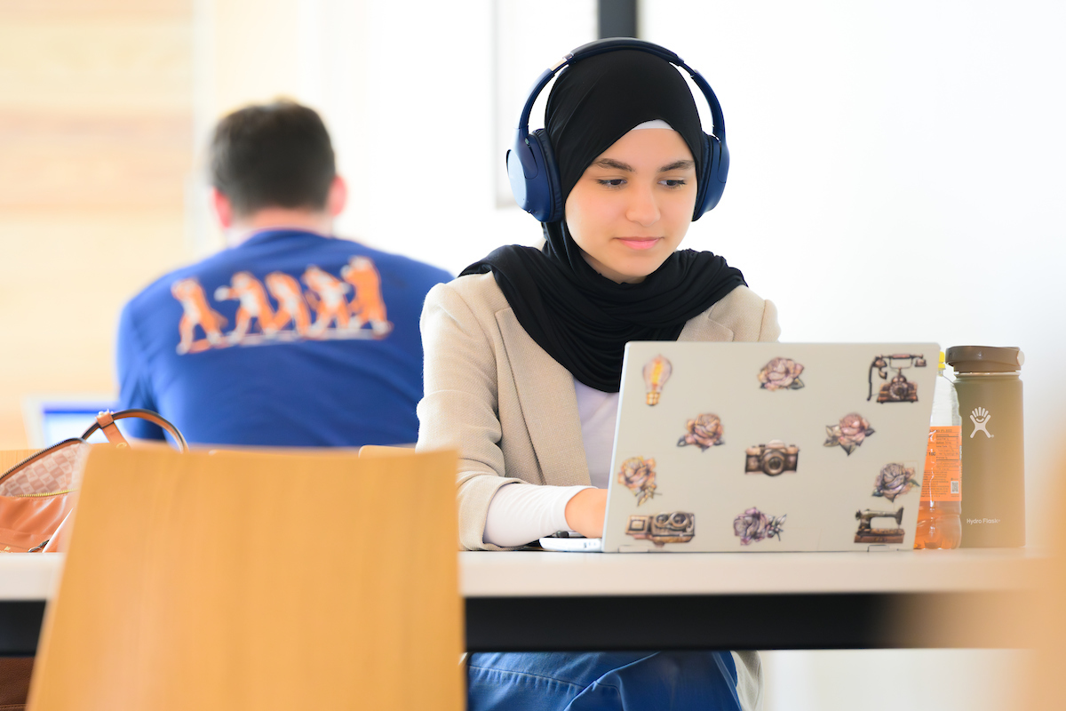 student working on laptop at a table in a common space