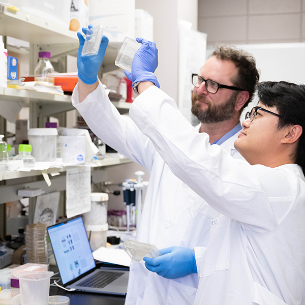 Faculty and graduate student working in lab together, wearing white coats