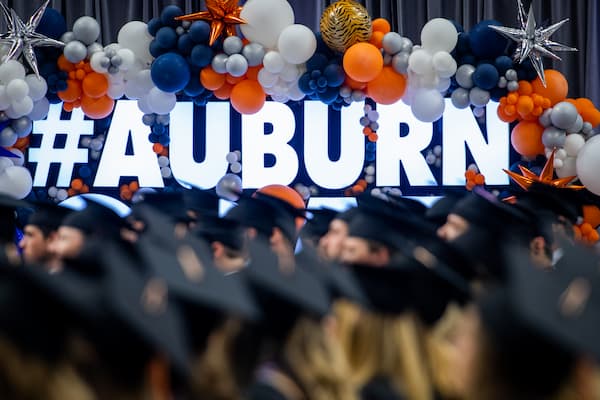 student wearing graduation robe taking a selfie with aubie the tiger mascot