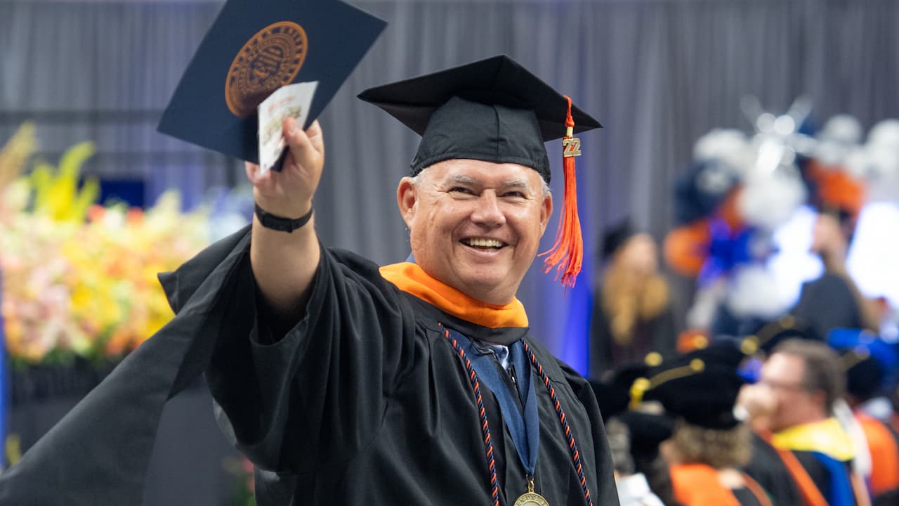man smiling with diploma at graduation