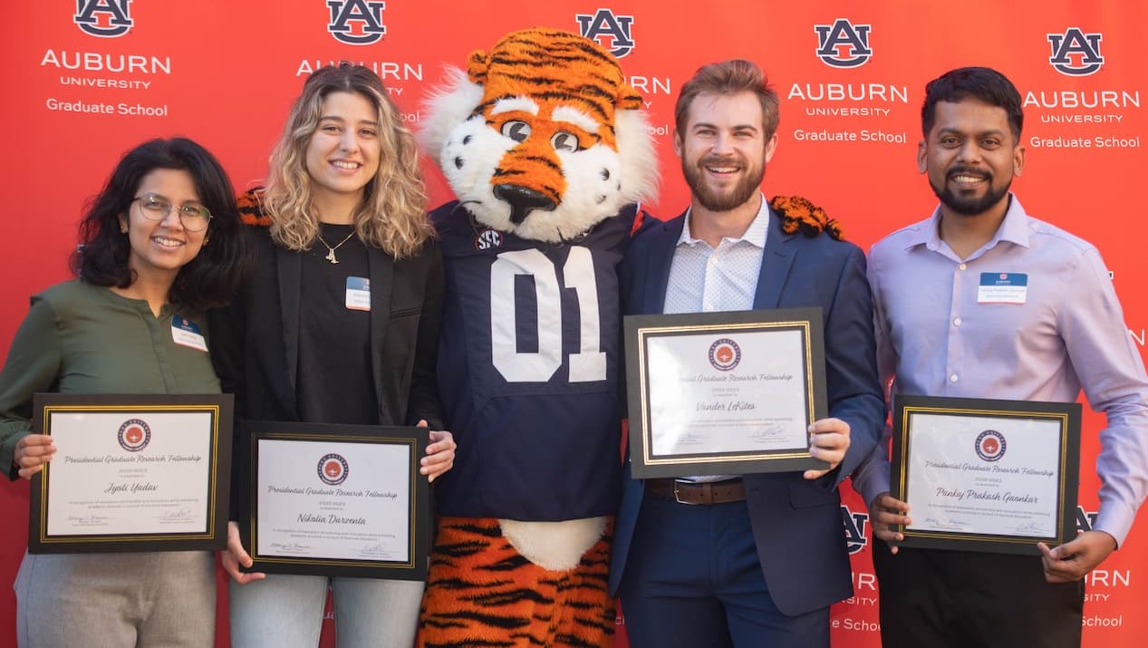 four students with award certificates pose for a photo with Aubie the Tiger mascot in front of an orange AU backdrop