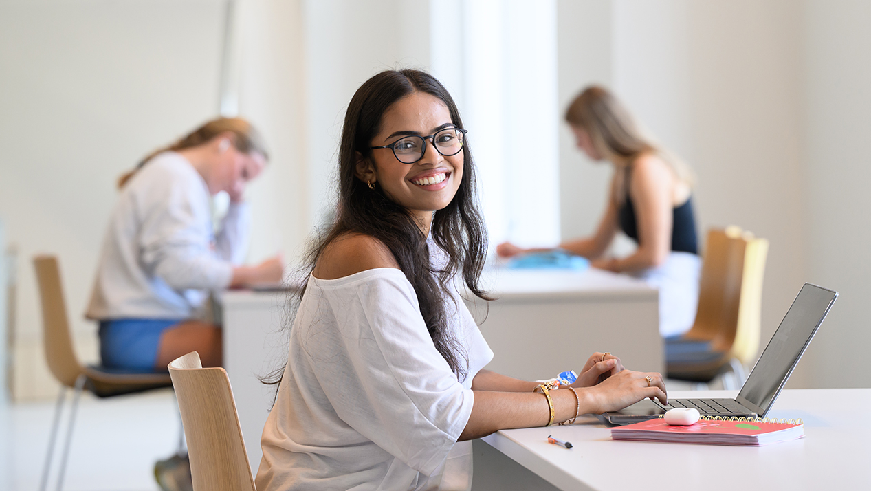student with laptop sitting at study table in academic building