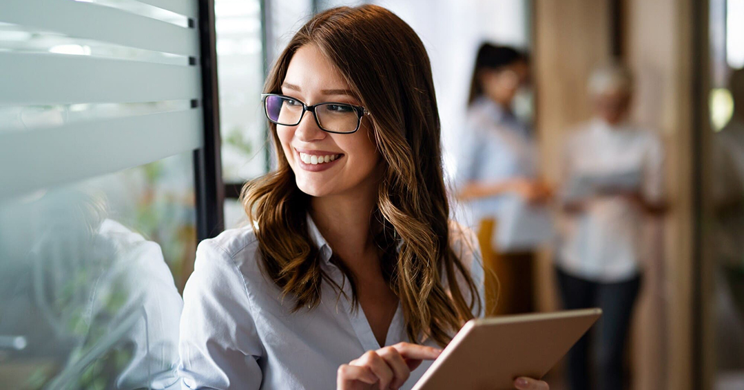 Woman holding a tablet and smiling confidently while in an office setting