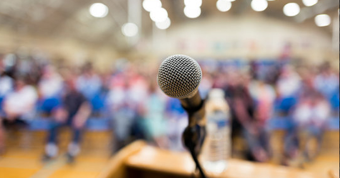 microphone at a podium in front of a large lecture hall full of people